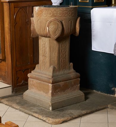Zdjęcie nr 2: Piaskowcowa, płaskorzeźbiona chrzcielnica ustawiona na prostopadłościennym, profilowanym postumencie z uskokiem. Trzon o przekroju ośmiobocznym dekorowany płaskorzeźbionym, symetrycznym ornamentem roślinnym. Czara półkolista, puklowana; w narożach owalne tarcze z godłami herbów: Odrowąż, Gryf, Drużyna i Warna oraz syglami „S(ebastian) L(ubomirski)”. W otoku czary ornament analogiczny jak na trzonie. Pokrywa drewniana o podstawie ośmiobocznej z dekoracją płycinową. Zwieńczona przecinającymi się kabłąkami dekorowanymi kaboszonami, zamknięta kulą oraz równoramiennym krzyżem o ramionach zakończonych trójlistnie. 