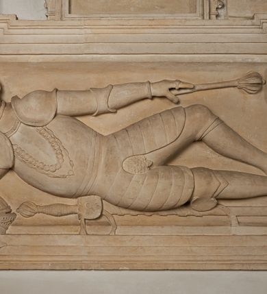 Zdjęcie nr 19: Nagrobek utworzony z dwóch położonych obok siebie płyt w formie leżącego prostokąta, w profilowanych, uszatych obramieniach z płaskorzeźbionymi, leżącymi postaciami Stanisława Lubomirskiego (po lewej) i Jakuba Lubomirskiego (po prawej). Postać po lewej leży na prawym boku, z ręką ugiętą i podpierającą głowę, zaś lewą ułożoną wzdłuż ciała, z buzdyganem w dłoni przyozdobionej pierścieniem, z ugiętą lewą nogą. Jego twarz jest pociągła, nos wydatny, ale krótki, oczy zamknięte. Włosy ma krótkie, lekko kręcone. Ubrany jest w zbroję typu husarskiego, składającą się z napierśnika z dwoma folgami brzusznymi pod szyją zakończonego wysokim kołnierzem, z naramienników, nałokietników, z sześciofolgowych taszek, nakolanników, nagolenników i butów. Na piersi zawieszony ma łańcuch. Pod nim leży hełm z pióropuszem i długi miecz. W prawym, górnym rogu kartusz z owalnym wypukłym polem z godłem herbu Drużyna i syglami w polu &quot;S&quot; i &quot;L&quot;. Nad nim kamienna tablica. 
Na prawej płycie ukazano Jakuba Lubomirskiego, leżącego na lewym boku, na ugiętej, lewej ręce i prawej ułożonej wzdłuż ciała, z księgą pod dłonią. Jego twarz jest pociągła, nos krótki, oczy zamknięte. Twarz okala długa, falista broda i wąsy, na głowie włosy sięgające uszu. Postać jest ubrana w albę i komżę. Nad płytą kamienna tablica z inskrypcją: „FVNEBRE CARME(NI) INTVMVLO REVE(REN)/DI D(OMI)NI IACOBI LVBOMIERSKI IMPRIME(N)DV(M). 
Nagrobek wieńczy czteropolowy kartusz z herbami: Drużyna, Odrowąż (Ogończyk), Warnia (Rak) i Gryf. Nad kartuszem hełm z koroną z zawieszonym u szyi krzyżem kawalerskim i ujęty labrami. 
