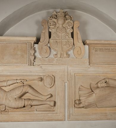 Zdjęcie nr 13: Nagrobek utworzony z dwóch położonych obok siebie płyt w formie leżącego prostokąta, w profilowanych, uszatych obramieniach z płaskorzeźbionymi, leżącymi postaciami Stanisława Lubomirskiego (po lewej) i Jakuba Lubomirskiego (po prawej). Postać po lewej leży na prawym boku, z ręką ugiętą i podpierającą głowę, zaś lewą ułożoną wzdłuż ciała, z buzdyganem w dłoni przyozdobionej pierścieniem, z ugiętą lewą nogą. Jego twarz jest pociągła, nos wydatny, ale krótki, oczy zamknięte. Włosy ma krótkie, lekko kręcone. Ubrany jest w zbroję typu husarskiego, składającą się z napierśnika z dwoma folgami brzusznymi pod szyją zakończonego wysokim kołnierzem, z naramienników, nałokietników, z sześciofolgowych taszek, nakolanników, nagolenników i butów. Na piersi zawieszony ma łańcuch. Pod nim leży hełm z pióropuszem i długi miecz. W prawym, górnym rogu kartusz z owalnym wypukłym polem z godłem herbu Drużyna i syglami w polu &quot;S&quot; i &quot;L&quot;. Nad nim kamienna tablica. 
Na prawej płycie ukazano Jakuba Lubomirskiego, leżącego na lewym boku, na ugiętej, lewej ręce i prawej ułożonej wzdłuż ciała, z księgą pod dłonią. Jego twarz jest pociągła, nos krótki, oczy zamknięte. Twarz okala długa, falista broda i wąsy, na głowie włosy sięgające uszu. Postać jest ubrana w albę i komżę. Nad płytą kamienna tablica z inskrypcją: „FVNEBRE CARME(NI) INTVMVLO REVE(REN)/DI D(OMI)NI IACOBI LVBOMIERSKI IMPRIME(N)DV(M). 
Nagrobek wieńczy czteropolowy kartusz z herbami: Drużyna, Odrowąż (Ogończyk), Warnia (Rak) i Gryf. Nad kartuszem hełm z koroną z zawieszonym u szyi krzyżem kawalerskim i ujęty labrami. 
