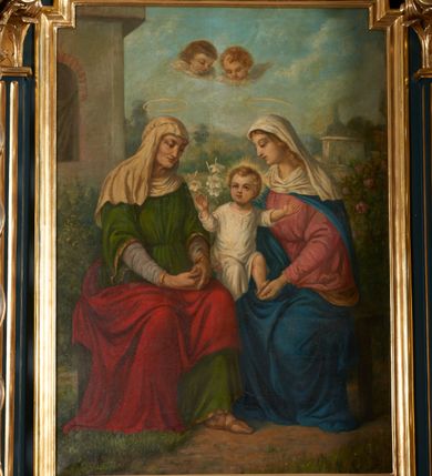 Zdjęcie nr 2: Obraz w kształcie stojącego prostokąta ze ściętymi schodkowo górnymi narożami, ujęty złoconą i profilowaną ramą. W centrum kompozycji  przedstawienie św. Anny Samotrzeć umieszczone na tle pejzażu z elementami architektury oraz roślinności. Święta Anna (po lewej), Maria (po prawej) siedzące na ławie, zwracają się ku sobie. Maria przedstawiona jako młoda, jasnowłosa kobieta ubrana w różową suknię oraz błękitny płaszcz podtrzymuje na kolanach Dzieciątko Jezus odziane w białą tunikę. Na głowie Marii i wokół jej szyi udrapowana biała chusta. Za Marią krzew kwitnących róż. Dzieciątko Jezus jasnowłose, ukazane w dynamicznej pozie z rękoma wyciągniętymi ku górze. Wokół jego głowy przedstawiony promienisty nimb. Za plecami Jezusa pęk białych lilii. Anna przedstawiona jako starsza kobieta w zielonej sukni, jasnofioletowej szacie spodniej, kremowej chuście na głowie oraz narzuconym na kolana czerwonym płaszczu. Dłonie kobiety splecione i swobodnie złożone na kolanach. Spod szat widoczna stopa w jasnobrązowym sandale. Ponad głowami Anny i Marii przedstawione aureole. W górnej części kompozycji, na osi obrazu widoczne dwie uskrzydlone główki anielskie. Kolorystyka jasna, pastelowa. W dolnej części obrazu, poniżej św. Anny umieszczona sygnatura malarza i data wykonania obrazu „18 FO 97.”