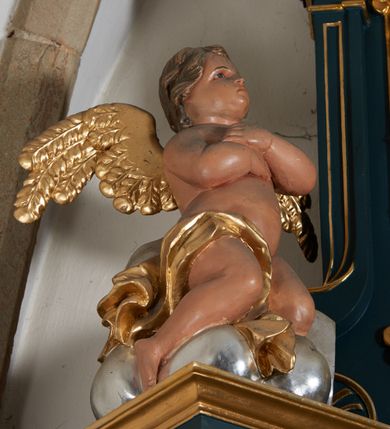 Zdjęcie nr 17: Ołtarz przyścienny, architektoniczny, dwukondygnacyjny, jednoosiowy. Mensa prostopadłościenna, antepedium haftowane z motywem serca gorejącego ujętego winnymi gronami oraz kłosami. Na  mensie architektoniczne, ujęte kolumnami tabernakulum z płaskorzeźbionym kielichem i hostią na drzwiczkach. W pierwszej kondygnacji obraz w kształcie stojącego prostokąta o uskokowo ściętych, górnych narożach z przedstawieniem św. Anny Samotrzeć (na zasuwie obraz „Najświętsze Serce Jezusa”) ujęty umieszczonymi na postumentach, kręconymi, złoconymi  i srebrzonymi kolumnami o kompozytowych kapitelach ustawionymi na tle kanelowanych pilastrów. Podpory dźwigają pełne, wyłamane belkowanie zwieńczone wydatnym, profilowanym gzymsem. Na osiach podpór pełnoplastyczne figury aniołów na obłokach. Fryz dekorowany rozetami oraz uskrzydloną główką anielską. W drugiej kondygnacji obraz św. Franciszka w ramie zamkniętej łukiem półkolistym wyniesionym, z uskokiem. Szczyt w formie przerwanego przyczółka, na osi którego krzyż. Całość nastawy ujęta ażurowymi uszami uformowanymi  z suchego akantu oraz wstęgi. Dekoracja akantowa, rozety, pola wypełnione kratą. Struktura nastawy w odcieniu ciemnej, morskiej zieleni, ornament złocony i srebrzony. 