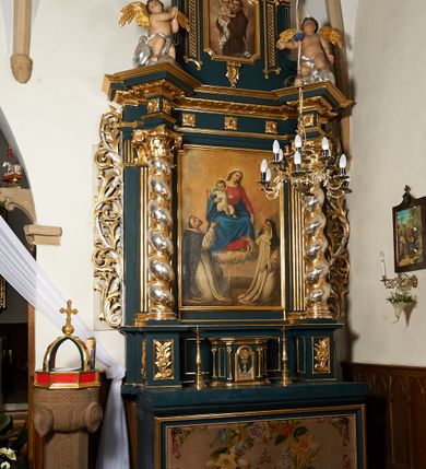 Zdjęcie nr 2: Ołtarz przyścienny, architektoniczny, dwukondygnacyjny, jednoosiowy. Mensa prostopadłościenna, antepedium haftowane w motyw kwiatowy z monogramem maryjnym. Na mensie architektoniczne, ujęte zdwojonymi, złoconymi kolumienkami tabernakulum z płaskorzeźbionym kielichem z hostią na drzwiczkach. W pierwszej kondygnacji obraz w kształcie stojącego prostokąta o uskokowo ściętych, górnych narożach z przedstawieniem Matki Boskiej Częstochowskiej oraz Matki Boskiej Różańcowej oraz św. Dominika i św. Katarzyny Sieneńskiej (na zasuwie). Kondygnacja ujęta umieszczonymi na postumentach, kręconymi, złoconymi  i srebrzonymi kolumnami o kompozytowych kapitelach ustawionymi na tle kanelowanych pilastrów. Podpory dźwigają pełne, wyłamane belkowanie zwieńczone wydatnym, profilowanym gzymsem. Na osiach podpór umieszczone pełnoplastyczne figury aniołów siedzących na obłokach. W drugiej kondygnacji obraz św. Antoniego Padewskiego w ramie zamkniętej łukiem półkolistym wyniesionym, z uskokiem. Szczyt w formie przerwanego przyczółka, na osi którego krzyż. Całość nastawy ujęta ażurowymi uszami uformowanymi z suchego akantu oraz wstęgi. Dekoracja akantowa, rozety, pola wypełnione kratą. Struktura nastawy w odcieniu ciemnej, morskiej zieleni, ornament złocony i srebrzony. Na portatylu nieczytelna odręczny napis z datą MDCCLXXII 1872.