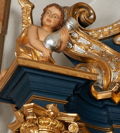 Zdjęcie nr 17: Ołtarz architektoniczny, trójosiowy, jednokondygnacyjny ze zwieńczeniem, na cokole. Mensa kamienna z portatylem. Antepedium proste, bez dekoracji, kamienne. Tabernakulum prostopadłościenne, ujęte pilastrami ustawionymi pod kątem, ze zwróconymi przeciwstawnie wolutami, zamiast trzonów, zwieńczone niepełnym belkowaniem. Drzwiczki w formie stojącego prostokąta zamkniętego łukiem półkolistym z krzyżem w polu. Retabulum ujęte parami pilastrów i kolumn o skręconych trzonach oraz kapitelach kompozytowych, dźwigających niepełne belkowanie z wydatnym gzymsem, wyłamanym w osiach podpór, przerwane w polu środkowym. Na gzymsie para puttów trzymających arma Christi. Osie boczne ustawione pod kątem względem lica ołtarza, w nich ustawiony dwie figury stojących aniołów. W polu środkowym ołtarza rama w formie stojącego prostokąta mieszcząca obraz św. Teresy z Lisieux. Zwieńczenie ołtarza w kształcie owalnego medalionu ujętego wydatnymi spływami wolutowymi. W polu owalny obraz przedstawiający wskrzeszenie Piotrowina. Kondygnacja pierwsza nastawy ujęta uszami utworzonymi z akantu. Cokoły podpór ozdobione z trzech stron płycinami z dekoracją roślinną w postaci liści i kwiatów. Na osi pilastrów cokoły podparte potrójną wolutą i parą girland owocowych. Trzony pilastrów i osie boczne dekorowane płycinami. Trzony kolumn zdobione ornamentem roślinnym. W polu środkowym ołtarza rama obrazu dekorowana akantem; u jej spodu akant i uskrzydlona główka anielska, zwieńczona akantem z palmetą. W zwieńczeniu profilowana rama dekorowana miejscami akantem, ujęta muszlą; woluty i lizeny zdobione kampanulami. Struktura ołtarza polichromowana na ciemnogranatowo ze złoconymi i srebrzonymi elementami architektonicznymi i ornamentyką.