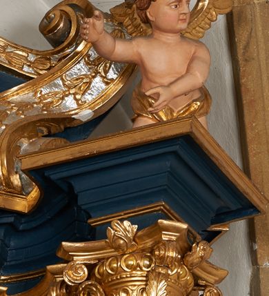 Zdjęcie nr 19: Ołtarz architektoniczny, trójosiowy, jednokondygnacyjny ze zwieńczeniem, na cokole. Mensa kamienna z portatylem. Antepedium proste, bez dekoracji, kamienne. Tabernakulum prostopadłościenne, ujęte pilastrami ustawionymi pod kątem, ze zwróconymi przeciwstawnie wolutami, zamiast trzonów, zwieńczone niepełnym belkowaniem. Drzwiczki w formie stojącego prostokąta zamkniętego łukiem półkolistym z krzyżem w polu. Retabulum ujęte parami pilastrów i kolumn o skręconych trzonach oraz kapitelach kompozytowych, dźwigających niepełne belkowanie z wydatnym gzymsem, wyłamanym w osiach podpór, przerwane w polu środkowym. Na gzymsie para puttów trzymających arma Christi. Osie boczne ustawione pod kątem względem lica ołtarza, w nich ustawiony dwie figury stojących aniołów. W polu środkowym ołtarza rama w formie stojącego prostokąta mieszcząca obraz św. Teresy z Lisieux. Zwieńczenie ołtarza w kształcie owalnego medalionu ujętego wydatnymi spływami wolutowymi. W polu owalny obraz przedstawiający wskrzeszenie Piotrowina. Kondygnacja pierwsza nastawy ujęta uszami utworzonymi z akantu. Cokoły podpór ozdobione z trzech stron płycinami z dekoracją roślinną w postaci liści i kwiatów. Na osi pilastrów cokoły podparte potrójną wolutą i parą girland owocowych. Trzony pilastrów i osie boczne dekorowane płycinami. Trzony kolumn zdobione ornamentem roślinnym. W polu środkowym ołtarza rama obrazu dekorowana akantem; u jej spodu akant i uskrzydlona główka anielska, zwieńczona akantem z palmetą. W zwieńczeniu profilowana rama dekorowana miejscami akantem, ujęta muszlą; woluty i lizeny zdobione kampanulami. Struktura ołtarza polichromowana na ciemnogranatowo ze złoconymi i srebrzonymi elementami architektonicznymi i ornamentyką.