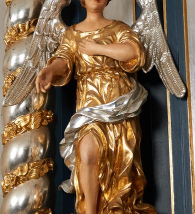 Zdjęcie nr 12: Ołtarz architektoniczny, trójosiowy, jednokondygnacyjny ze zwieńczeniem, na cokole. Mensa kamienna z portatylem. Antepedium proste, bez dekoracji, kamienne. Tabernakulum prostopadłościenne, ujęte pilastrami ustawionymi pod kątem, ze zwróconymi przeciwstawnie wolutami, zamiast trzonów, zwieńczone niepełnym belkowaniem. Drzwiczki w formie stojącego prostokąta zamkniętego łukiem półkolistym z krzyżem w polu. Retabulum ujęte parami pilastrów i kolumn o skręconych trzonach oraz kapitelach kompozytowych, dźwigających niepełne belkowanie z wydatnym gzymsem, wyłamanym w osiach podpór, przerwane w polu środkowym. Na gzymsie para puttów trzymających arma Christi. Osie boczne ustawione pod kątem względem lica ołtarza, w nich ustawiony dwie figury stojących aniołów. W polu środkowym ołtarza rama w formie stojącego prostokąta mieszcząca obraz św. Teresy z Lisieux. Zwieńczenie ołtarza w kształcie owalnego medalionu ujętego wydatnymi spływami wolutowymi. W polu owalny obraz przedstawiający wskrzeszenie Piotrowina. Kondygnacja pierwsza nastawy ujęta uszami utworzonymi z akantu. Cokoły podpór ozdobione z trzech stron płycinami z dekoracją roślinną w postaci liści i kwiatów. Na osi pilastrów cokoły podparte potrójną wolutą i parą girland owocowych. Trzony pilastrów i osie boczne dekorowane płycinami. Trzony kolumn zdobione ornamentem roślinnym. W polu środkowym ołtarza rama obrazu dekorowana akantem; u jej spodu akant i uskrzydlona główka anielska, zwieńczona akantem z palmetą. W zwieńczeniu profilowana rama dekorowana miejscami akantem, ujęta muszlą; woluty i lizeny zdobione kampanulami. Struktura ołtarza polichromowana na ciemnogranatowo ze złoconymi i srebrzonymi elementami architektonicznymi i ornamentyką.