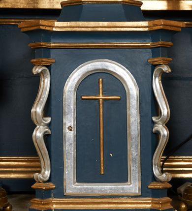 Zdjęcie nr 23: Ołtarz architektoniczny, trójosiowy, jednokondygnacyjny ze zwieńczeniem, na cokole. Mensa kamienna z portatylem. Antepedium proste, bez dekoracji, kamienne. Tabernakulum prostopadłościenne, ujęte pilastrami ustawionymi pod kątem, ze zwróconymi przeciwstawnie wolutami, zamiast trzonów, zwieńczone niepełnym belkowaniem. Drzwiczki w formie stojącego prostokąta zamkniętego łukiem półkolistym z krzyżem w polu. Retabulum ujęte parami pilastrów i kolumn o skręconych trzonach oraz kapitelach kompozytowych, dźwigających niepełne belkowanie z wydatnym gzymsem, wyłamanym w osiach podpór, przerwane w polu środkowym. Na gzymsie para puttów trzymających arma Christi. Osie boczne ustawione pod kątem względem lica ołtarza, w nich ustawiony dwie figury stojących aniołów. W polu środkowym ołtarza rama w formie stojącego prostokąta mieszcząca obraz św. Teresy z Lisieux. Zwieńczenie ołtarza w kształcie owalnego medalionu ujętego wydatnymi spływami wolutowymi. W polu owalny obraz przedstawiający wskrzeszenie Piotrowina. Kondygnacja pierwsza nastawy ujęta uszami utworzonymi z akantu. Cokoły podpór ozdobione z trzech stron płycinami z dekoracją roślinną w postaci liści i kwiatów. Na osi pilastrów cokoły podparte potrójną wolutą i parą girland owocowych. Trzony pilastrów i osie boczne dekorowane płycinami. Trzony kolumn zdobione ornamentem roślinnym. W polu środkowym ołtarza rama obrazu dekorowana akantem; u jej spodu akant i uskrzydlona główka anielska, zwieńczona akantem z palmetą. W zwieńczeniu profilowana rama dekorowana miejscami akantem, ujęta muszlą; woluty i lizeny zdobione kampanulami. Struktura ołtarza polichromowana na ciemnogranatowo ze złoconymi i srebrzonymi elementami architektonicznymi i ornamentyką.