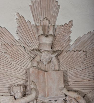 Zdjęcie nr 3: Naroża portalu do kaplicy ujęte wieńcami lauru i liśćmi akantu. Nad wejściem trzy putta trzymające otwartą księgę na tle monumentalnej glorii promienistej i obłoków. 
