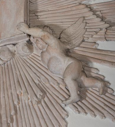 Zdjęcie nr 5: Naroża portalu do kaplicy ujęte wieńcami lauru i liśćmi akantu. Nad wejściem trzy putta trzymające otwartą księgę na tle monumentalnej glorii promienistej i obłoków. 