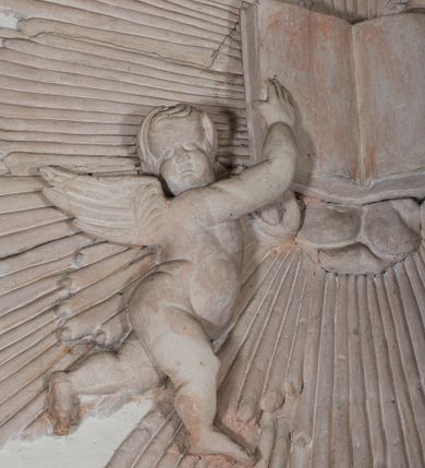 Zdjęcie nr 4: Naroża portalu do kaplicy ujęte wieńcami lauru i liśćmi akantu. Nad wejściem trzy putta trzymające otwartą księgę na tle monumentalnej glorii promienistej i obłoków. 