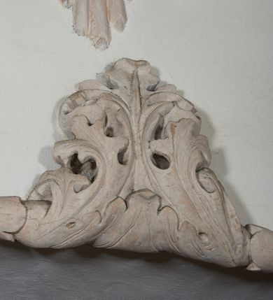 Zdjęcie nr 7: Naroża portalu do kaplicy ujęte wieńcami lauru i liśćmi akantu. Nad wejściem trzy putta trzymające otwartą księgę na tle monumentalnej glorii promienistej i obłoków. 