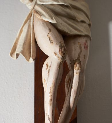 Zdjęcie nr 4: Krucyfiks drewniany, figura pełnoplastyczna, w pełni polichromowana. Ciało Chrystusa muskularne z silnie zaznaczoną anatomią klatki piersiowej i widocznymi śladami męki. Ramiona tworzące zarys litery „V”, prawa dłoń złożona w gest błogosławieństwa, lewa z wyprostowanym palcem wskazującym; stopy przebite jednym gwoździem. Głowa zwrócona w trzech czwartych w prawo, pochylona lekko do dołu. Twarz szczupła, pociągła, oczy zamknięte. Na głowie cierniowa korona, spod której ciekną krople krwi. Włosy i zarost ciemnobrązowe, kręcone. Perizonium białe, związane w węzeł na prawym boku postaci. U szczytu pionowej belki krzyża banderola z inskrypcją: „I.N./R.I.”