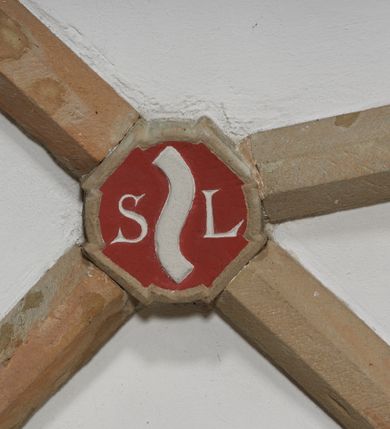 Zdjęcie nr 2: Komplet sześciu kamiennych konsol w formie męskich, brodatych głów, na które spływają żebra krzyżowego sklepienia w nawie głównej. Postać pierwsza o twarzy szerokiej, okolonej długim zarostem oraz włosami układającymi się w loki na czole. Oczy zamknięte, wydatny, prosty nos. Widoczne rurkowate bruzdy na czole. Postać druga o twarzy pociągłej, okolonej długim zarostem artykułowanym za pomocą rurkowatych fałd. Broda na końcu nieznacznie rozdwojona. Włosy proste ponad czołem tworzą trójkątne zakola. Oczy zamknięte, czoło pokryte bruzdami. Postać trzecia o trójkątnej twarzy z niskim, pokrytym bruzdami czołem i kręconych włosach. Oczy zamknięte. Postać czwarta o owalnej, pełnej twarzy, wystających kościach policzkowych. Zarost artykułowany za pomocą równoległych fałdek. Włosy układające się w loki ponad czołem. Oczy zamknięte. Postać piąta o szerokiej, płaskiej twarzy z gęstym zarostem. Długie, falowane wąsy, zamknięte oczy. Włosy ponad czołem układające się w loki. Postać szósta o pociągłej, podłużnej twarzy z zarostem. Długi, prosty nos, zamknięte oczy, niskie czoło ponad, którym bujne, proste włosy. Na przecięciach żeber dwa polichromowane zworniki z godłem herbu Drużyna oraz syglami „S(ebastian) L(ubomirski)" umieszczonymi na czerwonym tle, pierwszy ośmioboczny, drugi w kształcie wieloliścia. W podniebiu arkady tęczowej wolutowa konsola ustawiona na kapitelu pilastra w podniebiu łuku tęczowego. U podstawy konsoli, na osi umieszczony rollwerkowy kartusz mieszczący godło herbu Drużyna oraz sygle „S(ebastian) L(ubomirski)”. 