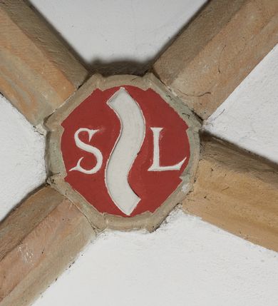 Zdjęcie nr 4: Komplet sześciu kamiennych konsol w formie męskich, brodatych głów, na które spływają żebra krzyżowego sklepienia w nawie głównej. Postać pierwsza o twarzy szerokiej, okolonej długim zarostem oraz włosami układającymi się w loki na czole. Oczy zamknięte, wydatny, prosty nos. Widoczne rurkowate bruzdy na czole. Postać druga o twarzy pociągłej, okolonej długim zarostem artykułowanym za pomocą rurkowatych fałd. Broda na końcu nieznacznie rozdwojona. Włosy proste ponad czołem tworzą trójkątne zakola. Oczy zamknięte, czoło pokryte bruzdami. Postać trzecia o trójkątnej twarzy z niskim, pokrytym bruzdami czołem i kręconych włosach. Oczy zamknięte. Postać czwarta o owalnej, pełnej twarzy, wystających kościach policzkowych. Zarost artykułowany za pomocą równoległych fałdek. Włosy układające się w loki ponad czołem. Oczy zamknięte. Postać piąta o szerokiej, płaskiej twarzy z gęstym zarostem. Długie, falowane wąsy, zamknięte oczy. Włosy ponad czołem układające się w loki. Postać szósta o pociągłej, podłużnej twarzy z zarostem. Długi, prosty nos, zamknięte oczy, niskie czoło ponad, którym bujne, proste włosy. Na przecięciach żeber dwa polichromowane zworniki z godłem herbu Drużyna oraz syglami „S(ebastian) L(ubomirski)" umieszczonymi na czerwonym tle, pierwszy ośmioboczny, drugi w kształcie wieloliścia. W podniebiu arkady tęczowej wolutowa konsola ustawiona na kapitelu pilastra w podniebiu łuku tęczowego. U podstawy konsoli, na osi umieszczony rollwerkowy kartusz mieszczący godło herbu Drużyna oraz sygle „S(ebastian) L(ubomirski)”. 