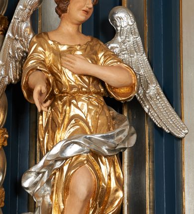 Zdjęcie nr 3: Para pełnoplastycznych, drążonych od tyłu, polichromowanych, złoconych i srebrzonych rzeźb przedstawiających stojące anioły w dynamicznych pozach. Figury przedstawione w kontrapoście, ustawione na niewielkich postumentach. Ubrane w długie, bogato drapowane, złocone suknie oraz rozwiane srebrzone płaszcze. Stopy bose. Obie postaci wykonują analogiczne gesty, składając jedną rękę na piersi, drugą wyciągając lekko do przodu. Twarze owalne, pełne z wydatnymi policzkami oraz podbródkami okolone jasnobrązowymi, kręconymi włosami. Karnacje polichromowane, skrzydła srebrzone.