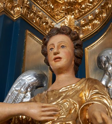 Zdjęcie nr 11: Para pełnoplastycznych, drążonych od tyłu, polichromowanych, złoconych i srebrzonych rzeźb przedstawiających stojące anioły w dynamicznych pozach. Figury przedstawione w kontrapoście, ustawione na niewielkich postumentach. Ubrane w długie, bogato drapowane, złocone suknie oraz rozwiane srebrzone płaszcze. Stopy bose. Obie postaci wykonują analogiczne gesty, składając jedną rękę na piersi, drugą wyciągając lekko do przodu. Twarze owalne, pełne z wydatnymi policzkami oraz podbródkami okolone jasnobrązowymi, kręconymi włosami. Karnacje polichromowane, skrzydła srebrzone.