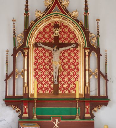 Zdjęcie nr 1: Ołtarz przyścienny, architektoniczny, jednokondygnacyjny, jednoosiowy. Mensa drewniana, prostopadłościenna na cokole. Antepedium dekorowane płyciną w formie leżącego prostokąta mieszczącą medalion z monogramem IHS w otoku z glorii promienistej. Retabulum o neogotyckich formach umieszczone na niewielkim cokole z monogramem PX na osi. W centrum ostrołukowa płycina ujęta złoconymi neogotyckimi kolumienkami mieszcząca rzeźbiony krucyfiks. W tle malowana dekoracja w postaci wici roślinnej oraz równoramiennych krzyży. Całość ujęta ażurowymi uszami w formie ostrołukowych, wypełnionych maswerkiem arkadek zwieńczonych pinaklami. Całość zamknięta od góry wimpergą zdobioną złoconymi żabkami oraz zwieńczoną krzyżem. Struktura malowana w odcieniach brązu, zieleni i czerwieni. Detal architektoniczny oraz ornamentyka złocone.