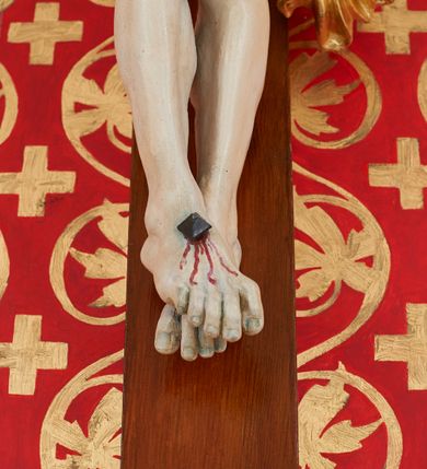 Zdjęcie nr 4: Pełnoplastyczna, polichromowana figura przedstawiająca ukrzyżowanego Chrystusa. Ciało muskularne o dobrze oddanej budowie anatomicznej z wyeksponowaną raną w prawym boku postaci. Głowa okolona długimi, brązowymi włosami, w cierniowej, złoconej koronie, opuszczona w dół i skierowana lekko w prawo. Twarz podłużna z zamkniętymi oczami, długim, prostym nosem oraz lekko rozchylonymi, sinymi ustami. Perizonium krótkie, złocone, udrapowane na lewym boku postaci. Stopy przebite jednym gwoździem. U szczytu pionowej belki krzyża złocony titulus z napisem „IN/RI”.