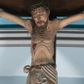 Zdjęcie nr 1: Krucyfiks z rzeźbą Chrystusa przybitą do krzyża trzema gwoździami. Figura zawieszona na szeroko rozłożonych, wyprężonych ramionach, w niewielkim zwisie. Sylwetka szczupła, o wyraźnie podkreślonej linii żeber i mostka. Głowa opada nieznacznie w kierunku prawego barku. Twarz podłużna, okolona krótką brodą, z zamkniętymi oczami; włosy długie, spływające na prawe ramię; na głowie korona cierniowa. Perizonium białe, przewiązane sznurem, odsłaniające prawe udo. Na ciele widoczne liczne strużki krwi spływające z ran. Krzyż prosty, gładki, ciemnobrązowy. Nad głową Chrystusa tabliczka w formie białej banderoli z napisem „IN / RI”.
