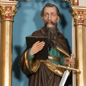 Zdjęcie nr 1: Rzeźba św. Pawła ustawiona na niskim prostopadłościennym cokole o ściętych narożach. Święty Paweł ustawiony frontalnie, w delikatnym kontrapoście, z lewą nogą ugiętą w kolanie. W prawej dłoni trzyma otwartą księgę, a w lewej miecz. Twarz o jasnej karnacji, z długim i szerokim nosem, okolona długą i bujną brodą. Włosy ciemnobrązowe, gęste, zaczesane do tyłu. Ubrany jest w zieloną suknię z długimi rękawami oraz ciemnobrązowy płaszcz ze złotą podszewką, zdobiony na brzegach złoconym pasem. Księga w czarnej obwolucie. Polichromia w odsłoniętych partiach ciała naturalistyczna, detale złocone i srebrzone.

