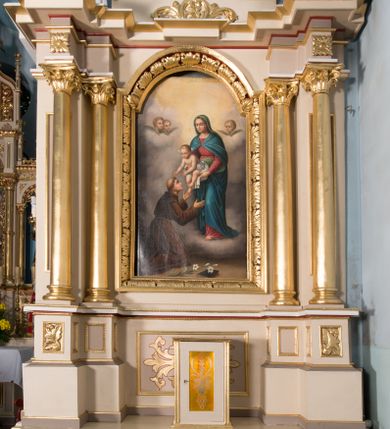 Zdjęcie nr 1: Nastawa ołtarzowa architektoniczna, jednoosiowa, jednokondygnacyjna ze zwieńczeniem. Ołtarz prostopadłościenny, drewniany; mensa drewniana. Antepedium w kształcie leżącego prostokąta ujętego profilowaną ramą; w polu płycina z malowaną i złoconą dekoracją roślinną flankującą medalion z krzyżem równoramiennym. Tabernakulum w formie prostopadłościennej skrzynki. Drzwiczki o kształcie stojącego prostokąta z płyciną dekorowaną malowanym i złoconym przedstawieniem kiści i liścia winnego grona oraz symetrycznego kłosa. Predella dekorowana płyciną z malowaną i złoconą dekoracją stylizowanego akantu. Nastawa ołtarzowa ustawiona na zdwojonym cokole, ujęta dwiema parami kolumn o kapitelach kompozytowych, z których zewnętrzna para wysunięta jest do przodu i ustawiona na tle filarów. Cokoły zdobione są płycinami o karbowanych ramach, na osi zewnętrznych podpór z płaskorzeźbionym liściem. Podpory dźwigają niepełne belkowanie składające się z fryzu i silnie wysuniętego gzymsu, wyłamane na ich osi; nad polem środkowym połączone gzymsem oraz przerwany trójkątny przyczółek z siedzącą na nim parą aniołów. W polu znajduje się ozdobna rama w kształcie stojącego prostokąta, zamkniętego łukiem nadwieszonym z obrazem św. Antoniego Padewskiego z Matką Boską z Dzieciątkiem. Zwieńczenie w kształcie stojącego prostokąta, zamknięte łukiem półkolistym, ustawione na wysokim cokole, ujęte parą kolumn o kapitelach kompozytowych podtrzymujących przerwany przyczółek; po bokach flankowane spływami wolutowymi. U szczytu akroterion w formie neorokokowej dekoracji roślinnej. W polu obraz św. Franciszka przed Chrystusem w ramie powtarzającej kształt zwieńczenia. Struktura w całości polichromowana w kolorze jasnobeżowym; kolumny, ornamentyka i profile złocone.