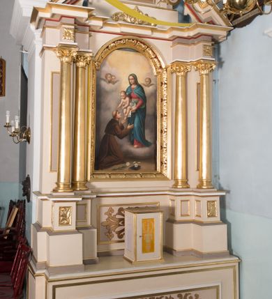 Zdjęcie nr 2: Nastawa ołtarzowa architektoniczna, jednoosiowa, jednokondygnacyjna ze zwieńczeniem. Ołtarz prostopadłościenny, drewniany; mensa drewniana. Antepedium w kształcie leżącego prostokąta ujętego profilowaną ramą; w polu płycina z malowaną i złoconą dekoracją roślinną flankującą medalion z krzyżem równoramiennym. Tabernakulum w formie prostopadłościennej skrzynki. Drzwiczki o kształcie stojącego prostokąta z płyciną dekorowaną malowanym i złoconym przedstawieniem kiści i liścia winnego grona oraz symetrycznego kłosa. Predella dekorowana płyciną z malowaną i złoconą dekoracją stylizowanego akantu. Nastawa ołtarzowa ustawiona na zdwojonym cokole, ujęta dwiema parami kolumn o kapitelach kompozytowych, z których zewnętrzna para wysunięta jest do przodu i ustawiona na tle filarów. Cokoły zdobione są płycinami o karbowanych ramach, na osi zewnętrznych podpór z płaskorzeźbionym liściem. Podpory dźwigają niepełne belkowanie składające się z fryzu i silnie wysuniętego gzymsu, wyłamane na ich osi; nad polem środkowym połączone gzymsem oraz przerwany trójkątny przyczółek z siedzącą na nim parą aniołów. W polu znajduje się ozdobna rama w kształcie stojącego prostokąta, zamkniętego łukiem nadwieszonym z obrazem św. Antoniego Padewskiego z Matką Boską z Dzieciątkiem. Zwieńczenie w kształcie stojącego prostokąta, zamknięte łukiem półkolistym, ustawione na wysokim cokole, ujęte parą kolumn o kapitelach kompozytowych podtrzymujących przerwany przyczółek; po bokach flankowane spływami wolutowymi. U szczytu akroterion w formie neorokokowej dekoracji roślinnej. W polu obraz św. Franciszka przed Chrystusem w ramie powtarzającej kształt zwieńczenia. Struktura w całości polichromowana w kolorze jasnobeżowym; kolumny, ornamentyka i profile złocone.
