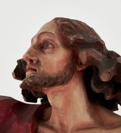 Zdjęcie nr 12: Pełnoplastyczna figura Chrystusa Zmartwychwstałego ustawiona na prostopadłościennym postumencie o ściętych narożach. Chrystus ukazany w pozycji stojącej, w wykroku, z prawą nogą wysuniętą do przodu. Na stopie widoczna rana po gwoździach. Prawa ręka postaci uniesiona, lewa trzymająca drzewiec Chorągwi Zmartwychwstania zwieńczony krzyżem. Głowa Chrystusa lekko uniesiona, zwrócona w prawą stronę. Twarz pociągła o wyrazistych, ostrych rysach, okolona długimi, falowanymi, rozwianymi włosami i krótką, rozwidloną brodą. Chrystus ubrany w obszerny, czerwony płaszcz o głęboko rzeźbionych fałdach, z rozwianą połą przy prawym ramieniu. Figura polichromowana, drzewiec chorągwi złocony.