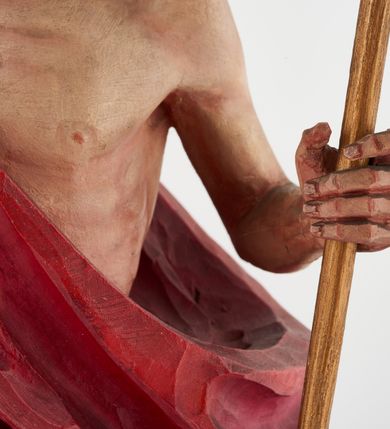 Zdjęcie nr 4: Pełnoplastyczna figura Chrystusa Zmartwychwstałego ustawiona na prostopadłościennym postumencie o ściętych narożach. Chrystus ukazany w pozycji stojącej, w wykroku, z prawą nogą wysuniętą do przodu. Na stopie widoczna rana po gwoździach. Prawa ręka postaci uniesiona, lewa trzymająca drzewiec Chorągwi Zmartwychwstania zwieńczony krzyżem. Głowa Chrystusa lekko uniesiona, zwrócona w prawą stronę. Twarz pociągła o wyrazistych, ostrych rysach, okolona długimi, falowanymi, rozwianymi włosami i krótką, rozwidloną brodą. Chrystus ubrany w obszerny, czerwony płaszcz o głęboko rzeźbionych fałdach, z rozwianą połą przy prawym ramieniu. Figura polichromowana, drzewiec chorągwi złocony.