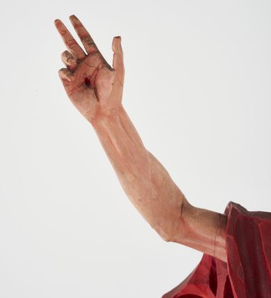 Zdjęcie nr 3: Pełnoplastyczna figura Chrystusa Zmartwychwstałego ustawiona na prostopadłościennym postumencie o ściętych narożach. Chrystus ukazany w pozycji stojącej, w wykroku, z prawą nogą wysuniętą do przodu. Na stopie widoczna rana po gwoździach. Prawa ręka postaci uniesiona, lewa trzymająca drzewiec Chorągwi Zmartwychwstania zwieńczony krzyżem. Głowa Chrystusa lekko uniesiona, zwrócona w prawą stronę. Twarz pociągła o wyrazistych, ostrych rysach, okolona długimi, falowanymi, rozwianymi włosami i krótką, rozwidloną brodą. Chrystus ubrany w obszerny, czerwony płaszcz o głęboko rzeźbionych fałdach, z rozwianą połą przy prawym ramieniu. Figura polichromowana, drzewiec chorągwi złocony.