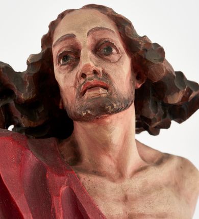 Zdjęcie nr 11: Pełnoplastyczna figura Chrystusa Zmartwychwstałego ustawiona na prostopadłościennym postumencie o ściętych narożach. Chrystus ukazany w pozycji stojącej, w wykroku, z prawą nogą wysuniętą do przodu. Na stopie widoczna rana po gwoździach. Prawa ręka postaci uniesiona, lewa trzymająca drzewiec Chorągwi Zmartwychwstania zwieńczony krzyżem. Głowa Chrystusa lekko uniesiona, zwrócona w prawą stronę. Twarz pociągła o wyrazistych, ostrych rysach, okolona długimi, falowanymi, rozwianymi włosami i krótką, rozwidloną brodą. Chrystus ubrany w obszerny, czerwony płaszcz o głęboko rzeźbionych fałdach, z rozwianą połą przy prawym ramieniu. Figura polichromowana, drzewiec chorągwi złocony.