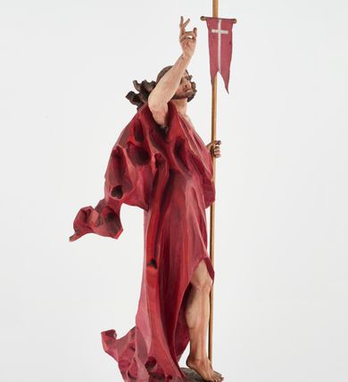 Zdjęcie nr 8: Pełnoplastyczna figura Chrystusa Zmartwychwstałego ustawiona na prostopadłościennym postumencie o ściętych narożach. Chrystus ukazany w pozycji stojącej, w wykroku, z prawą nogą wysuniętą do przodu. Na stopie widoczna rana po gwoździach. Prawa ręka postaci uniesiona, lewa trzymająca drzewiec Chorągwi Zmartwychwstania zwieńczony krzyżem. Głowa Chrystusa lekko uniesiona, zwrócona w prawą stronę. Twarz pociągła o wyrazistych, ostrych rysach, okolona długimi, falowanymi, rozwianymi włosami i krótką, rozwidloną brodą. Chrystus ubrany w obszerny, czerwony płaszcz o głęboko rzeźbionych fałdach, z rozwianą połą przy prawym ramieniu. Figura polichromowana, drzewiec chorągwi złocony.