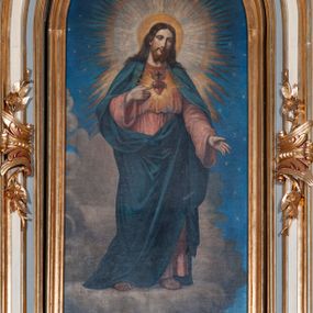Zdjęcie nr 1: Obraz w kształcie stojącego prostokąta z przedstawieniem Najświętszego Serca Jezusa ujęty złotą, profilowaną ramą. W centrum kompozycji Chrystus ukazany w całej postaci. Prawą ręką wskazuje na gorejące, koronowane cierniem serce umieszczone na jego piersi, lewą ma opuszczoną, głowę przechyla na lewe ramię, patrzy na widza. Ma owalną twarz o smutnym wyrazie, brązowe oczy, wąski nos i niewielkie usta, na policzkach delikatny rumieniec. Długie, brązowe włosy spływają mu na ramiona i plecy, twarz okala rozdzielona w dwa pukle broda i wąsy. Wokół głowy szeroki, promienisty nimb w różnych odcieniach żółtego koloru. Chrystus jest ubrany w długą, jasnoczerwoną suknię przepasaną sznurem, a na nią ma zarzucony ciemnoniebieski płaszcz, który zakrywa nogi, ramiona i jest zaczepiony o pasek przy lewym biodrze. Zbawiciel stoi na i pośród chmur, w tle gwieździste niebo. Kolorystyka obrazu jasna, pastelowa.   
