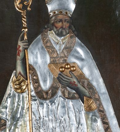 Zdjęcie nr 1: Obraz z wizerunkiem św. Mikołaja, ukazanego w całej postaci, frontalnie, w stroju przykrytym srebrną, miejscami złoconą  sukienką. Twarz okolona siwą brodą, nos prosty, oczy ciemne otwarte. Święty jest ubrany w srebrną albę, dekorowaną pasem złotej koronki, stułę i kapę z szerokimi złotymi brzegami, którą ma spiętą pod szyją. Na głowie ma infułę, na dłoniach długie rękawiczki, na stopach buty; rękawiczki i buty są zdobione czerwonymi krzyżami. W prawej ręce trzyma pastorał, a lewą przytrzymuje zamkniętą, złotą księgę z trzema złotymi kulami leżącymi na oprawie. Przy lewej krawędzi płótna, na dole postać tego samego świętego ponad cembrzykiem, w którym stoi trzech nagich młodzieńców.  Tło jednolite, ciemne. Obraz ujęty cienką, profilowaną, złoconą ramą. 