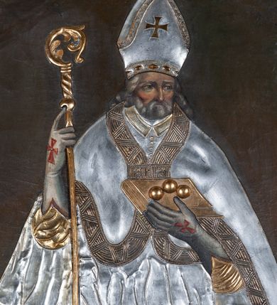 Zdjęcie nr 2: Obraz z wizerunkiem św. Mikołaja, ukazanego w całej postaci, frontalnie, w stroju przykrytym srebrną, miejscami złoconą  sukienką. Twarz okolona siwą brodą, nos prosty, oczy ciemne otwarte. Święty jest ubrany w srebrną albę, dekorowaną pasem złotej koronki, stułę i kapę z szerokimi złotymi brzegami, którą ma spiętą pod szyją. Na głowie ma infułę, na dłoniach długie rękawiczki, na stopach buty; rękawiczki i buty są zdobione czerwonymi krzyżami. W prawej ręce trzyma pastorał, a lewą przytrzymuje zamkniętą, złotą księgę z trzema złotymi kulami leżącymi na oprawie. Przy lewej krawędzi płótna, na dole postać tego samego świętego ponad cembrzykiem, w którym stoi trzech nagich młodzieńców.  Tło jednolite, ciemne. Obraz ujęty cienką, profilowaną, złoconą ramą. 