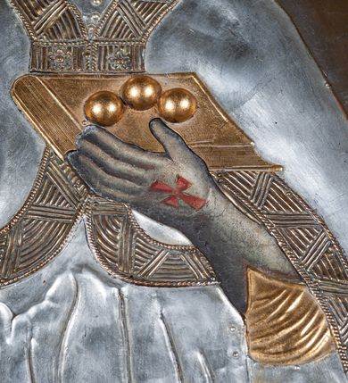 Zdjęcie nr 5: Obraz z wizerunkiem św. Mikołaja, ukazanego w całej postaci, frontalnie, w stroju przykrytym srebrną, miejscami złoconą  sukienką. Twarz okolona siwą brodą, nos prosty, oczy ciemne otwarte. Święty jest ubrany w srebrną albę, dekorowaną pasem złotej koronki, stułę i kapę z szerokimi złotymi brzegami, którą ma spiętą pod szyją. Na głowie ma infułę, na dłoniach długie rękawiczki, na stopach buty; rękawiczki i buty są zdobione czerwonymi krzyżami. W prawej ręce trzyma pastorał, a lewą przytrzymuje zamkniętą, złotą księgę z trzema złotymi kulami leżącymi na oprawie. Przy lewej krawędzi płótna, na dole postać tego samego świętego ponad cembrzykiem, w którym stoi trzech nagich młodzieńców.  Tło jednolite, ciemne. Obraz ujęty cienką, profilowaną, złoconą ramą. 