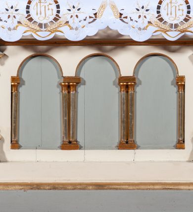 Zdjęcie nr 7: Ołtarz architektoniczny, jednokondygnacyjny, jednoosiowy, w formie aediculi, na podwójnym cokole oddzielonym linią gzymsu. Antepedium w formie leżącego prostokąta z trzema arkadami podtrzymywanymi przez kolumny toskańskie. Całość ujęta w dwie grube kolumny o kapitelach kompozytowych, stojące na cokołach. W narożach figury czterech istot apokaliptycznych: lwa, orła, anioła i wołu.  Pole środkowe nastawy flankowane jest dwiema parami kolumn na cokołach, o kapitelach kompozytowych. Wewnętrzna para kolumn została wysunięta nieco przed lico ołtarza i podtrzymuje półokrągłą arkadę. Całość zwieńczona gzymsem w formie łuku nadwieszonego, który w partii środkowej wyłamuje się, przybierając kształt prostokąta zwieńczonego trójkątnie. Cokoły dekorowane płycinami z ornamentem roślinnym, geometryczno-roślinnym i rozetami. Trzony kolumn kanelowane spiralnie, w połowie ujęte opaską, dekorowane guzami. Archiwolta arkady profilowana, ozdobiona maswerkiem. W polu środkowym obraz św. Mikołaja w profilowanej ramie z elementami geometrycznymi i liśćmi. W polu tympanonu płaskorzeźba z insygniami papieskimi – infułą, pastorałem, krzyżem patriarszym i kluczami. Powierzchnia ponad arkadą dekorowana kratką regencyjną z rozetami. Gzyms wieńczący ozdobiony rozetami i liśćmi oraz ażurowym akantem. Całość zwieńczona krzyżem. 
Struktura polichromowana na kolor kremowy, płyciny niebieskie i ciemnoczerwone, detale i ornamenty złocone i srebrzone. 
