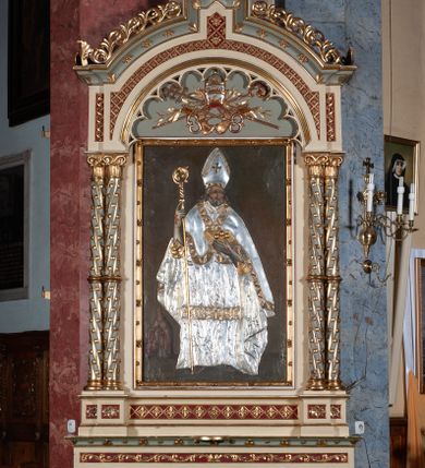 Zdjęcie nr 1: Ołtarz architektoniczny, jednokondygnacyjny, jednoosiowy, w formie aediculi, na podwójnym cokole oddzielonym linią gzymsu. Antepedium w formie leżącego prostokąta z trzema arkadami podtrzymywanymi przez kolumny toskańskie. Całość ujęta w dwie grube kolumny o kapitelach kompozytowych, stojące na cokołach. W narożach figury czterech istot apokaliptycznych: lwa, orła, anioła i wołu.  Pole środkowe nastawy flankowane jest dwiema parami kolumn na cokołach, o kapitelach kompozytowych. Wewnętrzna para kolumn została wysunięta nieco przed lico ołtarza i podtrzymuje półokrągłą arkadę. Całość zwieńczona gzymsem w formie łuku nadwieszonego, który w partii środkowej wyłamuje się, przybierając kształt prostokąta zwieńczonego trójkątnie. Cokoły dekorowane płycinami z ornamentem roślinnym, geometryczno-roślinnym i rozetami. Trzony kolumn kanelowane spiralnie, w połowie ujęte opaską, dekorowane guzami. Archiwolta arkady profilowana, ozdobiona maswerkiem. W polu środkowym obraz św. Mikołaja w profilowanej ramie z elementami geometrycznymi i liśćmi. W polu tympanonu płaskorzeźba z insygniami papieskimi – infułą, pastorałem, krzyżem patriarszym i kluczami. Powierzchnia ponad arkadą dekorowana kratką regencyjną z rozetami. Gzyms wieńczący ozdobiony rozetami i liśćmi oraz ażurowym akantem. Całość zwieńczona krzyżem. 
Struktura polichromowana na kolor kremowy, płyciny niebieskie i ciemnoczerwone, detale i ornamenty złocone i srebrzone. 
