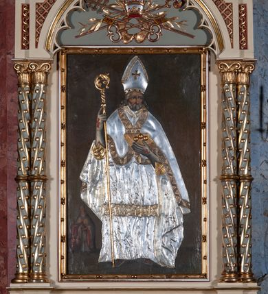 Zdjęcie nr 10: Ołtarz architektoniczny, jednokondygnacyjny, jednoosiowy, w formie aediculi, na podwójnym cokole oddzielonym linią gzymsu. Antepedium w formie leżącego prostokąta z trzema arkadami podtrzymywanymi przez kolumny toskańskie. Całość ujęta w dwie grube kolumny o kapitelach kompozytowych, stojące na cokołach. W narożach figury czterech istot apokaliptycznych: lwa, orła, anioła i wołu.  Pole środkowe nastawy flankowane jest dwiema parami kolumn na cokołach, o kapitelach kompozytowych. Wewnętrzna para kolumn została wysunięta nieco przed lico ołtarza i podtrzymuje półokrągłą arkadę. Całość zwieńczona gzymsem w formie łuku nadwieszonego, który w partii środkowej wyłamuje się, przybierając kształt prostokąta zwieńczonego trójkątnie. Cokoły dekorowane płycinami z ornamentem roślinnym, geometryczno-roślinnym i rozetami. Trzony kolumn kanelowane spiralnie, w połowie ujęte opaską, dekorowane guzami. Archiwolta arkady profilowana, ozdobiona maswerkiem. W polu środkowym obraz św. Mikołaja w profilowanej ramie z elementami geometrycznymi i liśćmi. W polu tympanonu płaskorzeźba z insygniami papieskimi – infułą, pastorałem, krzyżem patriarszym i kluczami. Powierzchnia ponad arkadą dekorowana kratką regencyjną z rozetami. Gzyms wieńczący ozdobiony rozetami i liśćmi oraz ażurowym akantem. Całość zwieńczona krzyżem. 
Struktura polichromowana na kolor kremowy, płyciny niebieskie i ciemnoczerwone, detale i ornamenty złocone i srebrzone. 
