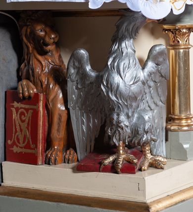 Zdjęcie nr 8: Ołtarz architektoniczny, jednokondygnacyjny, jednoosiowy, w formie aediculi, na podwójnym cokole oddzielonym linią gzymsu. Antepedium w formie leżącego prostokąta z trzema arkadami podtrzymywanymi przez kolumny toskańskie. Całość ujęta w dwie grube kolumny o kapitelach kompozytowych, stojące na cokołach. W narożach figury czterech istot apokaliptycznych: lwa, orła, anioła i wołu.  Pole środkowe nastawy flankowane jest dwiema parami kolumn na cokołach, o kapitelach kompozytowych. Wewnętrzna para kolumn została wysunięta nieco przed lico ołtarza i podtrzymuje półokrągłą arkadę. Całość zwieńczona gzymsem w formie łuku nadwieszonego, który w partii środkowej wyłamuje się, przybierając kształt prostokąta zwieńczonego trójkątnie. Cokoły dekorowane płycinami z ornamentem roślinnym, geometryczno-roślinnym i rozetami. Trzony kolumn kanelowane spiralnie, w połowie ujęte opaską, dekorowane guzami. Archiwolta arkady profilowana, ozdobiona maswerkiem. W polu środkowym obraz św. Mikołaja w profilowanej ramie z elementami geometrycznymi i liśćmi. W polu tympanonu płaskorzeźba z insygniami papieskimi – infułą, pastorałem, krzyżem patriarszym i kluczami. Powierzchnia ponad arkadą dekorowana kratką regencyjną z rozetami. Gzyms wieńczący ozdobiony rozetami i liśćmi oraz ażurowym akantem. Całość zwieńczona krzyżem. 
Struktura polichromowana na kolor kremowy, płyciny niebieskie i ciemnoczerwone, detale i ornamenty złocone i srebrzone. 
