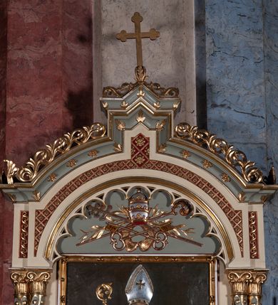 Zdjęcie nr 11: Ołtarz architektoniczny, jednokondygnacyjny, jednoosiowy, w formie aediculi, na podwójnym cokole oddzielonym linią gzymsu. Antepedium w formie leżącego prostokąta z trzema arkadami podtrzymywanymi przez kolumny toskańskie. Całość ujęta w dwie grube kolumny o kapitelach kompozytowych, stojące na cokołach. W narożach figury czterech istot apokaliptycznych: lwa, orła, anioła i wołu.  Pole środkowe nastawy flankowane jest dwiema parami kolumn na cokołach, o kapitelach kompozytowych. Wewnętrzna para kolumn została wysunięta nieco przed lico ołtarza i podtrzymuje półokrągłą arkadę. Całość zwieńczona gzymsem w formie łuku nadwieszonego, który w partii środkowej wyłamuje się, przybierając kształt prostokąta zwieńczonego trójkątnie. Cokoły dekorowane płycinami z ornamentem roślinnym, geometryczno-roślinnym i rozetami. Trzony kolumn kanelowane spiralnie, w połowie ujęte opaską, dekorowane guzami. Archiwolta arkady profilowana, ozdobiona maswerkiem. W polu środkowym obraz św. Mikołaja w profilowanej ramie z elementami geometrycznymi i liśćmi. W polu tympanonu płaskorzeźba z insygniami papieskimi – infułą, pastorałem, krzyżem patriarszym i kluczami. Powierzchnia ponad arkadą dekorowana kratką regencyjną z rozetami. Gzyms wieńczący ozdobiony rozetami i liśćmi oraz ażurowym akantem. Całość zwieńczona krzyżem. 
Struktura polichromowana na kolor kremowy, płyciny niebieskie i ciemnoczerwone, detale i ornamenty złocone i srebrzone. 
