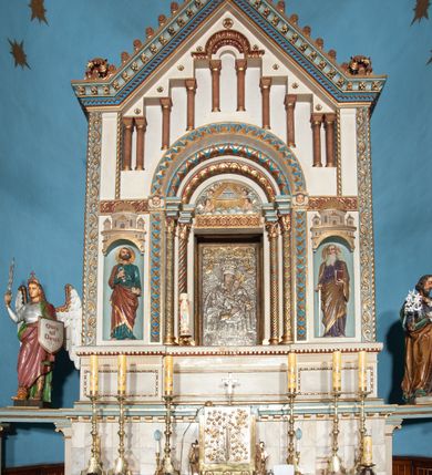 Zdjęcie nr 17: Ołtarz architektoniczny, jednokondygnacyjny, trójosiowy ze zwieńczeniem i bramkami, ustawiony na cokole. Mensa marmurowa z portatylem. Antepedium w formie wydłużonego, leżącego prostokąta. Ujęte w profilowaną ramę, podzielone na trzy części. Partia środkowa kwadratowa, w niej medalion z płaskorzeźbionym przedstawieniem gorejącego serca na tle skrzyżowanego krzyża i kotwicy. W partiach bocznych płaskorzeźbiony motyw maswerku. Na mensie prostopadłościenne tabernakulum z drzwiczkami dekorowanymi motywem silnie stylizowanych winnych gron, ustawione na cokole przerywanym trzema plakietami roślinnymi. Tabernakulum z dwóch stron podtrzymują stylizowane anioły. Pole środkowe nastawy ołtarza w formie uskokowego portalu zamkniętego półokrągłym łukiem z tympanonem. Dwie wewnętrzne archiwolty podtrzymywane przez półkolumny z kapitelami kompozytowymi, zewnętrzna przez pilastry. Portal flankują dwie nisze, zwieńczone łukiem nadwieszonym. Pierwszą kondygnację zamyka pas fryzu. W polu zwieńczenia ponad łukiem portalu rozchodzi się stopniowo pięć par kolumn o kostkowych kapitelach, które w partii wieńczącej podtrzymują profilowany łuk nadwieszony. Zwieńczenie zamknięte trójkątną linią belkowania, z pasem stopniowo spływających wolut, zakończone krzyżem. Cokół dekorowany płycinami z perełkowaniem, zakończony gzymsem z motywem wolich oczu. Poszczególne elementy niszy dekorowane różnorodnym ornamentem o charakterze geometryczno-roślinnym. W polu środkowym obraz Matki Boskiej z Dzieciątkiem w srebrnej sukience (Matki Boskiej Lisieckiej). W tympanonie płaskorzeźbione przedstawienie imienia Boga ujętego w trójkąt w glorii promienistej, w otoczeniu putt pośród obłoków. Nisze flankujące portal zwieńczone są płaskorzeźbionymi przedstawieniami centralnych świątyń kopułowych. W niszach płaskorzeźby św. Piotra po lewej i św. Pawła po prawej stronie. Fryz zamykający kondygnację z motywem palmet, w miejscu przecięcia z opaską portalu – uskrzydlone główki anielskie. W partii zwieńczenia, w przestrzeniach ponad kolumnami rozety. Ostatnia para kolumn ujęta w pionowe pasy imitujące zwinięty sznur. Łuk nadwieszony dekorowany ornamentem roślinnym. Cały ołtarz ujęty w pasy z dekoracją roślinną i motywem sznura. Wieńczące belkowanie z dekoracją geometryczną i rozetami, ujęte w woluty z mięsistego akantu. Podstawę dla krzyża tworzy akant z motywem palmety i perełkowania. Ołtarz flankują dwie bramki, na których stoją figury św. Michała Archanioła po lewej i św. Józefa po prawej stronie. 
Struktura w kolorze naturalnego kamienia – kremowa, profile w odcieniach niebieskiego, detale i ornamenty złocone. 
