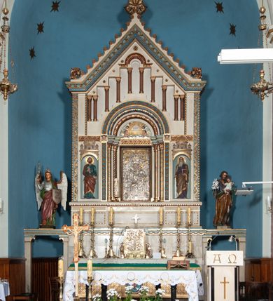 Zdjęcie nr 13: Ołtarz architektoniczny, jednokondygnacyjny, trójosiowy ze zwieńczeniem i bramkami, ustawiony na cokole. Mensa marmurowa z portatylem. Antepedium w formie wydłużonego, leżącego prostokąta. Ujęte w profilowaną ramę, podzielone na trzy części. Partia środkowa kwadratowa, w niej medalion z płaskorzeźbionym przedstawieniem gorejącego serca na tle skrzyżowanego krzyża i kotwicy. W partiach bocznych płaskorzeźbiony motyw maswerku. Na mensie prostopadłościenne tabernakulum z drzwiczkami dekorowanymi motywem silnie stylizowanych winnych gron, ustawione na cokole przerywanym trzema plakietami roślinnymi. Tabernakulum z dwóch stron podtrzymują stylizowane anioły. Pole środkowe nastawy ołtarza w formie uskokowego portalu zamkniętego półokrągłym łukiem z tympanonem. Dwie wewnętrzne archiwolty podtrzymywane przez półkolumny z kapitelami kompozytowymi, zewnętrzna przez pilastry. Portal flankują dwie nisze, zwieńczone łukiem nadwieszonym. Pierwszą kondygnację zamyka pas fryzu. W polu zwieńczenia ponad łukiem portalu rozchodzi się stopniowo pięć par kolumn o kostkowych kapitelach, które w partii wieńczącej podtrzymują profilowany łuk nadwieszony. Zwieńczenie zamknięte trójkątną linią belkowania, z pasem stopniowo spływających wolut, zakończone krzyżem. Cokół dekorowany płycinami z perełkowaniem, zakończony gzymsem z motywem wolich oczu. Poszczególne elementy niszy dekorowane różnorodnym ornamentem o charakterze geometryczno-roślinnym. W polu środkowym obraz Matki Boskiej z Dzieciątkiem w srebrnej sukience (Matki Boskiej Lisieckiej). W tympanonie płaskorzeźbione przedstawienie imienia Boga ujętego w trójkąt w glorii promienistej, w otoczeniu putt pośród obłoków. Nisze flankujące portal zwieńczone są płaskorzeźbionymi przedstawieniami centralnych świątyń kopułowych. W niszach płaskorzeźby św. Piotra po lewej i św. Pawła po prawej stronie. Fryz zamykający kondygnację z motywem palmet, w miejscu przecięcia z opaską portalu – uskrzydlone główki anielskie. W partii zwieńczenia, w przestrzeniach ponad kolumnami rozety. Ostatnia para kolumn ujęta w pionowe pasy imitujące zwinięty sznur. Łuk nadwieszony dekorowany ornamentem roślinnym. Cały ołtarz ujęty w pasy z dekoracją roślinną i motywem sznura. Wieńczące belkowanie z dekoracją geometryczną i rozetami, ujęte w woluty z mięsistego akantu. Podstawę dla krzyża tworzy akant z motywem palmety i perełkowania. Ołtarz flankują dwie bramki, na których stoją figury św. Michała Archanioła po lewej i św. Józefa po prawej stronie. 
Struktura w kolorze naturalnego kamienia – kremowa, profile w odcieniach niebieskiego, detale i ornamenty złocone. 
