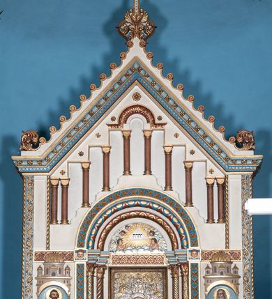 Zdjęcie nr 18: Ołtarz architektoniczny, jednokondygnacyjny, trójosiowy ze zwieńczeniem i bramkami, ustawiony na cokole. Mensa marmurowa z portatylem. Antepedium w formie wydłużonego, leżącego prostokąta. Ujęte w profilowaną ramę, podzielone na trzy części. Partia środkowa kwadratowa, w niej medalion z płaskorzeźbionym przedstawieniem gorejącego serca na tle skrzyżowanego krzyża i kotwicy. W partiach bocznych płaskorzeźbiony motyw maswerku. Na mensie prostopadłościenne tabernakulum z drzwiczkami dekorowanymi motywem silnie stylizowanych winnych gron, ustawione na cokole przerywanym trzema plakietami roślinnymi. Tabernakulum z dwóch stron podtrzymują stylizowane anioły. Pole środkowe nastawy ołtarza w formie uskokowego portalu zamkniętego półokrągłym łukiem z tympanonem. Dwie wewnętrzne archiwolty podtrzymywane przez półkolumny z kapitelami kompozytowymi, zewnętrzna przez pilastry. Portal flankują dwie nisze, zwieńczone łukiem nadwieszonym. Pierwszą kondygnację zamyka pas fryzu. W polu zwieńczenia ponad łukiem portalu rozchodzi się stopniowo pięć par kolumn o kostkowych kapitelach, które w partii wieńczącej podtrzymują profilowany łuk nadwieszony. Zwieńczenie zamknięte trójkątną linią belkowania, z pasem stopniowo spływających wolut, zakończone krzyżem. Cokół dekorowany płycinami z perełkowaniem, zakończony gzymsem z motywem wolich oczu. Poszczególne elementy niszy dekorowane różnorodnym ornamentem o charakterze geometryczno-roślinnym. W polu środkowym obraz Matki Boskiej z Dzieciątkiem w srebrnej sukience (Matki Boskiej Lisieckiej). W tympanonie płaskorzeźbione przedstawienie imienia Boga ujętego w trójkąt w glorii promienistej, w otoczeniu putt pośród obłoków. Nisze flankujące portal zwieńczone są płaskorzeźbionymi przedstawieniami centralnych świątyń kopułowych. W niszach płaskorzeźby św. Piotra po lewej i św. Pawła po prawej stronie. Fryz zamykający kondygnację z motywem palmet, w miejscu przecięcia z opaską portalu – uskrzydlone główki anielskie. W partii zwieńczenia, w przestrzeniach ponad kolumnami rozety. Ostatnia para kolumn ujęta w pionowe pasy imitujące zwinięty sznur. Łuk nadwieszony dekorowany ornamentem roślinnym. Cały ołtarz ujęty w pasy z dekoracją roślinną i motywem sznura. Wieńczące belkowanie z dekoracją geometryczną i rozetami, ujęte w woluty z mięsistego akantu. Podstawę dla krzyża tworzy akant z motywem palmety i perełkowania. Ołtarz flankują dwie bramki, na których stoją figury św. Michała Archanioła po lewej i św. Józefa po prawej stronie. 
Struktura w kolorze naturalnego kamienia – kremowa, profile w odcieniach niebieskiego, detale i ornamenty złocone. 
