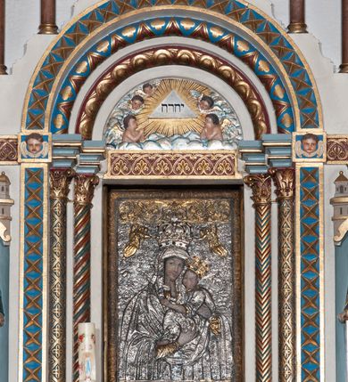 Zdjęcie nr 21: Ołtarz architektoniczny, jednokondygnacyjny, trójosiowy ze zwieńczeniem i bramkami, ustawiony na cokole. Mensa marmurowa z portatylem. Antepedium w formie wydłużonego, leżącego prostokąta. Ujęte w profilowaną ramę, podzielone na trzy części. Partia środkowa kwadratowa, w niej medalion z płaskorzeźbionym przedstawieniem gorejącego serca na tle skrzyżowanego krzyża i kotwicy. W partiach bocznych płaskorzeźbiony motyw maswerku. Na mensie prostopadłościenne tabernakulum z drzwiczkami dekorowanymi motywem silnie stylizowanych winnych gron, ustawione na cokole przerywanym trzema plakietami roślinnymi. Tabernakulum z dwóch stron podtrzymują stylizowane anioły. Pole środkowe nastawy ołtarza w formie uskokowego portalu zamkniętego półokrągłym łukiem z tympanonem. Dwie wewnętrzne archiwolty podtrzymywane przez półkolumny z kapitelami kompozytowymi, zewnętrzna przez pilastry. Portal flankują dwie nisze, zwieńczone łukiem nadwieszonym. Pierwszą kondygnację zamyka pas fryzu. W polu zwieńczenia ponad łukiem portalu rozchodzi się stopniowo pięć par kolumn o kostkowych kapitelach, które w partii wieńczącej podtrzymują profilowany łuk nadwieszony. Zwieńczenie zamknięte trójkątną linią belkowania, z pasem stopniowo spływających wolut, zakończone krzyżem. Cokół dekorowany płycinami z perełkowaniem, zakończony gzymsem z motywem wolich oczu. Poszczególne elementy niszy dekorowane różnorodnym ornamentem o charakterze geometryczno-roślinnym. W polu środkowym obraz Matki Boskiej z Dzieciątkiem w srebrnej sukience (Matki Boskiej Lisieckiej). W tympanonie płaskorzeźbione przedstawienie imienia Boga ujętego w trójkąt w glorii promienistej, w otoczeniu putt pośród obłoków. Nisze flankujące portal zwieńczone są płaskorzeźbionymi przedstawieniami centralnych świątyń kopułowych. W niszach płaskorzeźby św. Piotra po lewej i św. Pawła po prawej stronie. Fryz zamykający kondygnację z motywem palmet, w miejscu przecięcia z opaską portalu – uskrzydlone główki anielskie. W partii zwieńczenia, w przestrzeniach ponad kolumnami rozety. Ostatnia para kolumn ujęta w pionowe pasy imitujące zwinięty sznur. Łuk nadwieszony dekorowany ornamentem roślinnym. Cały ołtarz ujęty w pasy z dekoracją roślinną i motywem sznura. Wieńczące belkowanie z dekoracją geometryczną i rozetami, ujęte w woluty z mięsistego akantu. Podstawę dla krzyża tworzy akant z motywem palmety i perełkowania. Ołtarz flankują dwie bramki, na których stoją figury św. Michała Archanioła po lewej i św. Józefa po prawej stronie. 
Struktura w kolorze naturalnego kamienia – kremowa, profile w odcieniach niebieskiego, detale i ornamenty złocone. 
