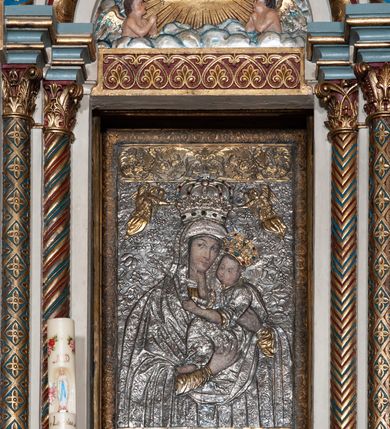 Zdjęcie nr 22: Ołtarz architektoniczny, jednokondygnacyjny, trójosiowy ze zwieńczeniem i bramkami, ustawiony na cokole. Mensa marmurowa z portatylem. Antepedium w formie wydłużonego, leżącego prostokąta. Ujęte w profilowaną ramę, podzielone na trzy części. Partia środkowa kwadratowa, w niej medalion z płaskorzeźbionym przedstawieniem gorejącego serca na tle skrzyżowanego krzyża i kotwicy. W partiach bocznych płaskorzeźbiony motyw maswerku. Na mensie prostopadłościenne tabernakulum z drzwiczkami dekorowanymi motywem silnie stylizowanych winnych gron, ustawione na cokole przerywanym trzema plakietami roślinnymi. Tabernakulum z dwóch stron podtrzymują stylizowane anioły. Pole środkowe nastawy ołtarza w formie uskokowego portalu zamkniętego półokrągłym łukiem z tympanonem. Dwie wewnętrzne archiwolty podtrzymywane przez półkolumny z kapitelami kompozytowymi, zewnętrzna przez pilastry. Portal flankują dwie nisze, zwieńczone łukiem nadwieszonym. Pierwszą kondygnację zamyka pas fryzu. W polu zwieńczenia ponad łukiem portalu rozchodzi się stopniowo pięć par kolumn o kostkowych kapitelach, które w partii wieńczącej podtrzymują profilowany łuk nadwieszony. Zwieńczenie zamknięte trójkątną linią belkowania, z pasem stopniowo spływających wolut, zakończone krzyżem. Cokół dekorowany płycinami z perełkowaniem, zakończony gzymsem z motywem wolich oczu. Poszczególne elementy niszy dekorowane różnorodnym ornamentem o charakterze geometryczno-roślinnym. W polu środkowym obraz Matki Boskiej z Dzieciątkiem w srebrnej sukience (Matki Boskiej Lisieckiej). W tympanonie płaskorzeźbione przedstawienie imienia Boga ujętego w trójkąt w glorii promienistej, w otoczeniu putt pośród obłoków. Nisze flankujące portal zwieńczone są płaskorzeźbionymi przedstawieniami centralnych świątyń kopułowych. W niszach płaskorzeźby św. Piotra po lewej i św. Pawła po prawej stronie. Fryz zamykający kondygnację z motywem palmet, w miejscu przecięcia z opaską portalu – uskrzydlone główki anielskie. W partii zwieńczenia, w przestrzeniach ponad kolumnami rozety. Ostatnia para kolumn ujęta w pionowe pasy imitujące zwinięty sznur. Łuk nadwieszony dekorowany ornamentem roślinnym. Cały ołtarz ujęty w pasy z dekoracją roślinną i motywem sznura. Wieńczące belkowanie z dekoracją geometryczną i rozetami, ujęte w woluty z mięsistego akantu. Podstawę dla krzyża tworzy akant z motywem palmety i perełkowania. Ołtarz flankują dwie bramki, na których stoją figury św. Michała Archanioła po lewej i św. Józefa po prawej stronie. 
Struktura w kolorze naturalnego kamienia – kremowa, profile w odcieniach niebieskiego, detale i ornamenty złocone. 
