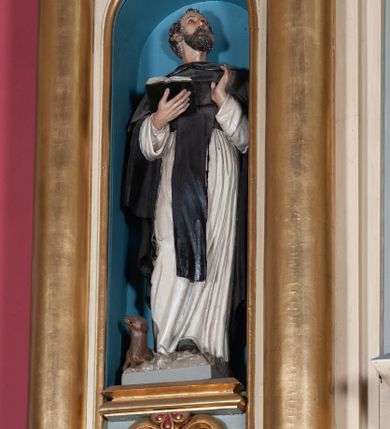 Zdjęcie nr 1: Rzeźba pełnoplastyczna, całopostaciowa, wydrążona od tyłu, na cokole.  Święty Dominik został ukazany frontalnie, w kontrapoście, z ciężarem na lewej nodze. W prawej ręce trzyma otwartą księgę, lewą unosi na wysokość torsu. Głowę ma uniesioną,  zwróconą w lewo, twarz pociągłą, okoloną krótką, brązową brodą i krótkimi, kręconymi włosami, czoło wysokie, wzrok skierowany ku górze. Święty jest ubrany w habit dominikański: białą tunikę przewiązaną czarnym pasem, czarny szkaplerz oraz długą czarną kapę i krótką pelerynkę. Przy prawej nodze świętego siedzi mały, brązowy pies, którzy szczerzy zęby. 
Polichromia w partiach ciała naturalistyczna.
