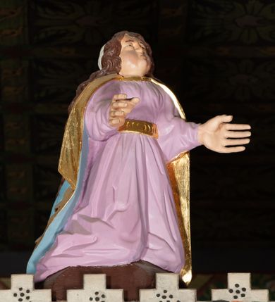 Zdjęcie nr 10: Trójfigurowa grupa Ukrzyżowania, rzeźby pełne. W środku znajduje się krucyfiks z postacią umarłego Chrystusa przybitego trzema gwoździami do krzyża. Chrystus w lekkim zwisie, o szeroko rozłożonych ramionach, bezwładny, głowa opuszczona na prawe ramię. Twarz szczupła, owalna, o prostym nosie, dużych oczach i na wpół otwartych ustach, okolona zarostem. Włosy w postaci delikatnych fal opadają na plecy i prawe ramię. Na głowie korona cierniowa. Ciało o wyraźnie zarysowanej anatomii. Perizonium w formie tkaniny przewiązanej na boku i odsłaniającej prawe biodro, z dłuższym brzegiem zwisającym po prawej stronie. Draperia gęsto fałdowana, o miękkich załamaniach materiału. Na szczycie pionowej belki titulus w formie banderoli z napisem „IN/RI”. Figura Matki Boskiej ustawiona po lewej stronie, zwrócona lekko w stronę krzyża, z głową uniesioną w kierunku Chrystusa i uniesionymi rękami. Twarz podłużna, niemal bez cech indywidualnych. Ubrana w długą białą suknię ze złotym paskiem, zielony płaszcz ze złotym podbiciem okrywający głowę, ramiona i plecy. Figura Marii Magdaleny po prawej stronie. Święta klęczy odwrócona od krzyża, z uniesioną głową i rozłożonymi rękami. Twarz młoda, owalna o słabo zindywidualizowanych rysach, włosy w postaci loków opadają na plecy. Jest ubrana w różową suknię ze złotym pasem oraz niebieski płaszcz ze złotym podbiciem. Polichromia w partiach ciała naturalistyczna. 