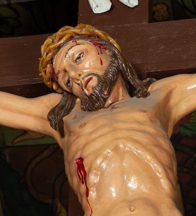 Zdjęcie nr 4: Trójfigurowa grupa Ukrzyżowania, rzeźby pełne. W środku znajduje się krucyfiks z postacią umarłego Chrystusa przybitego trzema gwoździami do krzyża. Chrystus w lekkim zwisie, o szeroko rozłożonych ramionach, bezwładny, głowa opuszczona na prawe ramię. Twarz szczupła, owalna, o prostym nosie, dużych oczach i na wpół otwartych ustach, okolona zarostem. Włosy w postaci delikatnych fal opadają na plecy i prawe ramię. Na głowie korona cierniowa. Ciało o wyraźnie zarysowanej anatomii. Perizonium w formie tkaniny przewiązanej na boku i odsłaniającej prawe biodro, z dłuższym brzegiem zwisającym po prawej stronie. Draperia gęsto fałdowana, o miękkich załamaniach materiału. Na szczycie pionowej belki titulus w formie banderoli z napisem „IN/RI”. Figura Matki Boskiej ustawiona po lewej stronie, zwrócona lekko w stronę krzyża, z głową uniesioną w kierunku Chrystusa i uniesionymi rękami. Twarz podłużna, niemal bez cech indywidualnych. Ubrana w długą białą suknię ze złotym paskiem, zielony płaszcz ze złotym podbiciem okrywający głowę, ramiona i plecy. Figura Marii Magdaleny po prawej stronie. Święta klęczy odwrócona od krzyża, z uniesioną głową i rozłożonymi rękami. Twarz młoda, owalna o słabo zindywidualizowanych rysach, włosy w postaci loków opadają na plecy. Jest ubrana w różową suknię ze złotym pasem oraz niebieski płaszcz ze złotym podbiciem. Polichromia w partiach ciała naturalistyczna. 