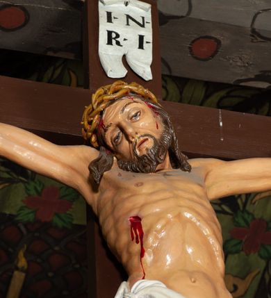 Zdjęcie nr 3: Trójfigurowa grupa Ukrzyżowania, rzeźby pełne. W środku znajduje się krucyfiks z postacią umarłego Chrystusa przybitego trzema gwoździami do krzyża. Chrystus w lekkim zwisie, o szeroko rozłożonych ramionach, bezwładny, głowa opuszczona na prawe ramię. Twarz szczupła, owalna, o prostym nosie, dużych oczach i na wpół otwartych ustach, okolona zarostem. Włosy w postaci delikatnych fal opadają na plecy i prawe ramię. Na głowie korona cierniowa. Ciało o wyraźnie zarysowanej anatomii. Perizonium w formie tkaniny przewiązanej na boku i odsłaniającej prawe biodro, z dłuższym brzegiem zwisającym po prawej stronie. Draperia gęsto fałdowana, o miękkich załamaniach materiału. Na szczycie pionowej belki titulus w formie banderoli z napisem „IN/RI”. Figura Matki Boskiej ustawiona po lewej stronie, zwrócona lekko w stronę krzyża, z głową uniesioną w kierunku Chrystusa i uniesionymi rękami. Twarz podłużna, niemal bez cech indywidualnych. Ubrana w długą białą suknię ze złotym paskiem, zielony płaszcz ze złotym podbiciem okrywający głowę, ramiona i plecy. Figura Marii Magdaleny po prawej stronie. Święta klęczy odwrócona od krzyża, z uniesioną głową i rozłożonymi rękami. Twarz młoda, owalna o słabo zindywidualizowanych rysach, włosy w postaci loków opadają na plecy. Jest ubrana w różową suknię ze złotym pasem oraz niebieski płaszcz ze złotym podbiciem. Polichromia w partiach ciała naturalistyczna. 