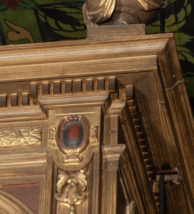 Zdjęcie nr 4: Organy architektoniczne, trójosiowe, na podwójnym cokole. Osie wydzielone pilastrami dźwigającymi gzyms z kostkowaniem. Środkowa wyższa niż boczne, zwieńczona trójkątnym, przerwanym przyczółkiem; pośrodku na gzymsie, rzeźbiona lira na cokole. Na osiach prześwity na piszczałki w formie stojącego prostokąta zamkniętego łukiem półkolistym, flankowanym przez półpilastry podtrzymujące profilowaną archiwoltę zwieńczoną kluczem; w osiach bocznych klucz w postaci liścia, w środkowej kartusz z głową. Zewnętrzne pilastry dekorowane kaboszonami i kampanulami, na gzymsie osi bocznych wazony. Struktura bejcowana w kolorze brązowym, ornamentyka złocona.