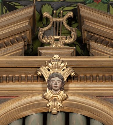 Zdjęcie nr 2: Organy architektoniczne, trójosiowe, na podwójnym cokole. Osie wydzielone pilastrami dźwigającymi gzyms z kostkowaniem. Środkowa wyższa niż boczne, zwieńczona trójkątnym, przerwanym przyczółkiem; pośrodku na gzymsie, rzeźbiona lira na cokole. Na osiach prześwity na piszczałki w formie stojącego prostokąta zamkniętego łukiem półkolistym, flankowanym przez półpilastry podtrzymujące profilowaną archiwoltę zwieńczoną kluczem; w osiach bocznych klucz w postaci liścia, w środkowej kartusz z głową. Zewnętrzne pilastry dekorowane kaboszonami i kampanulami, na gzymsie osi bocznych wazony. Struktura bejcowana w kolorze brązowym, ornamentyka złocona.